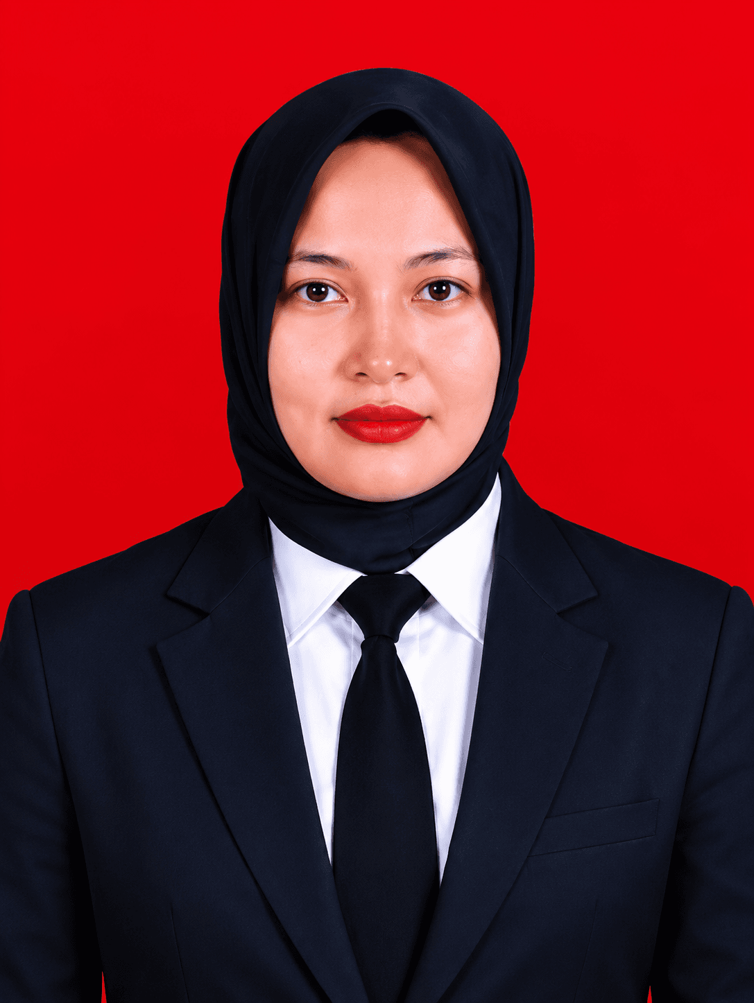 Wanita berhijab hitam mengenakan jas dan dasi hitam dengan latar belakang merah menyala.